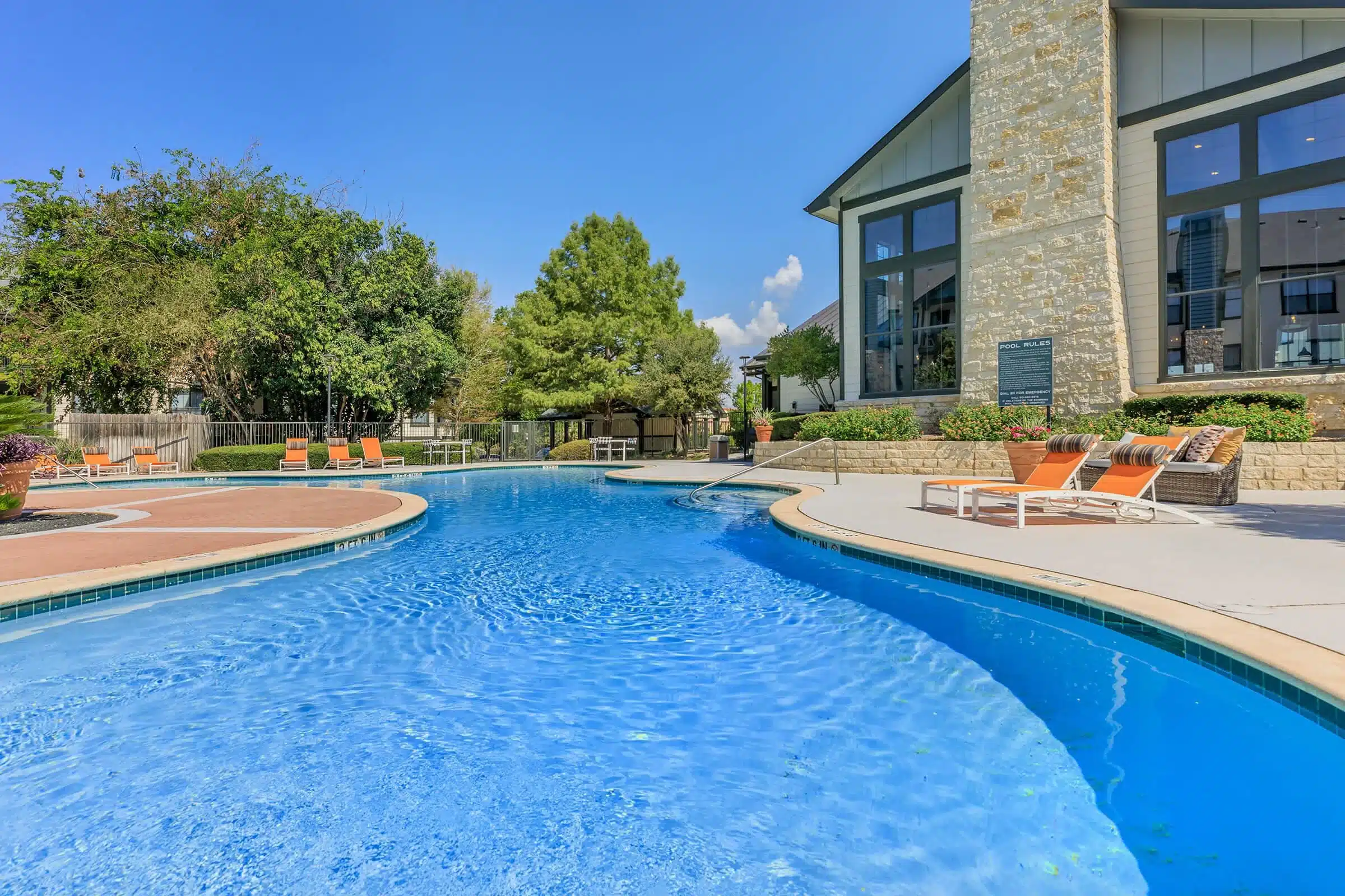 Outdoor swimming pool at The Heritage with clear blue water, lounge chairs, and trees under a sunny sky.