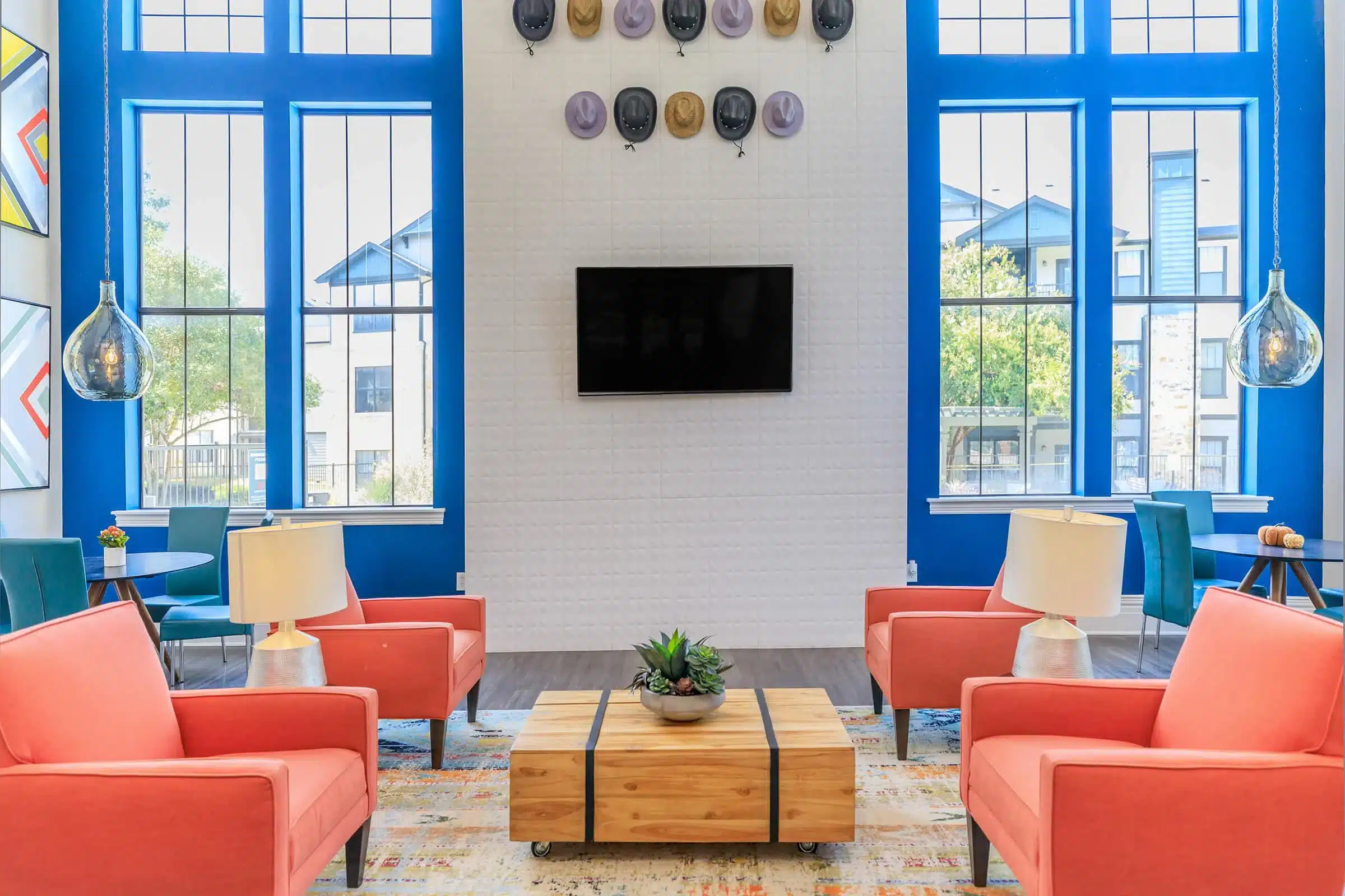 Modern lounge in The Heritage with coral armchairs, a wooden coffee table, blue walls, and hats displayed above a wall-mounted TV.