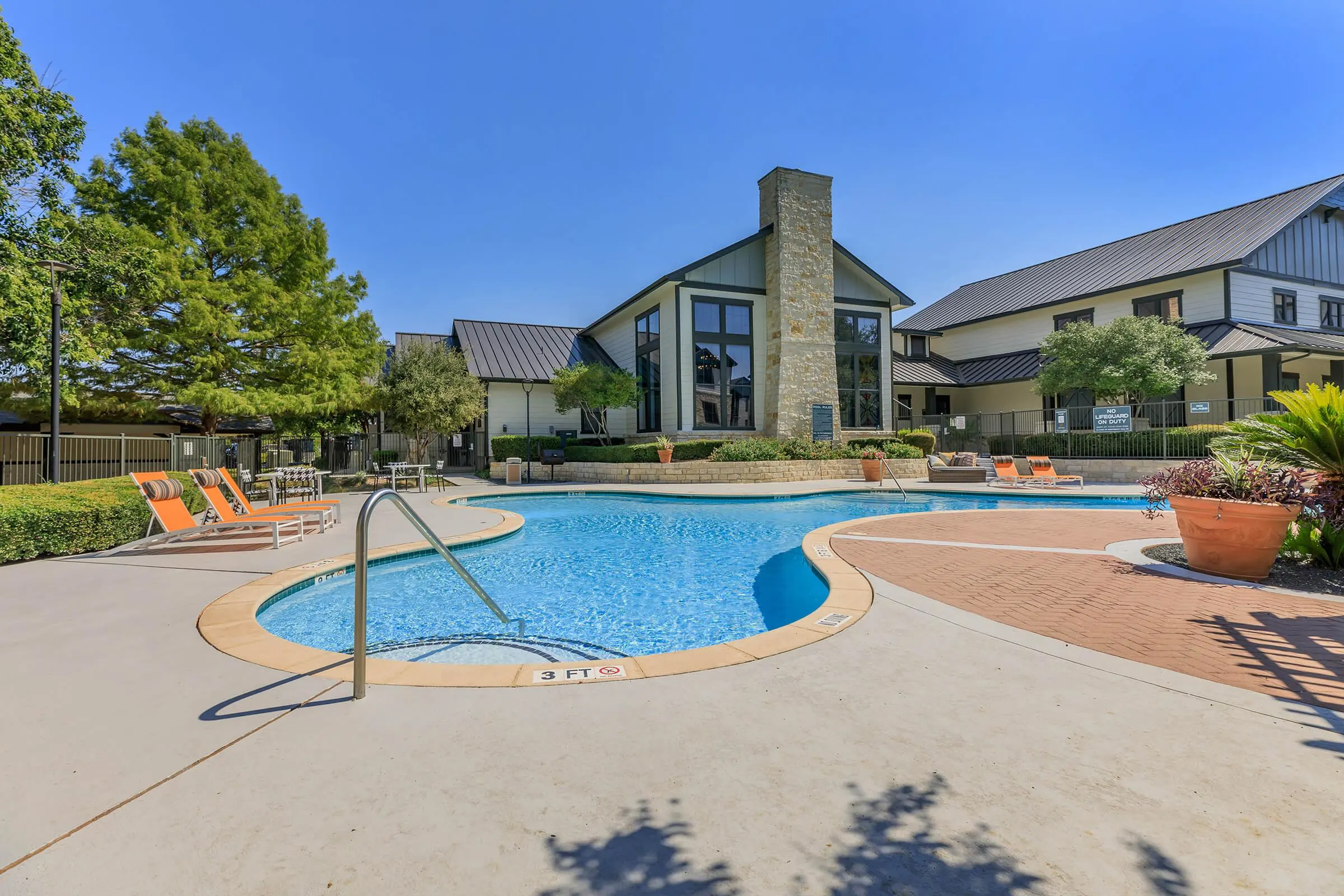 Outdoor swimming pool at The Heritage with lounge chairs and trees under a clear blue sky.