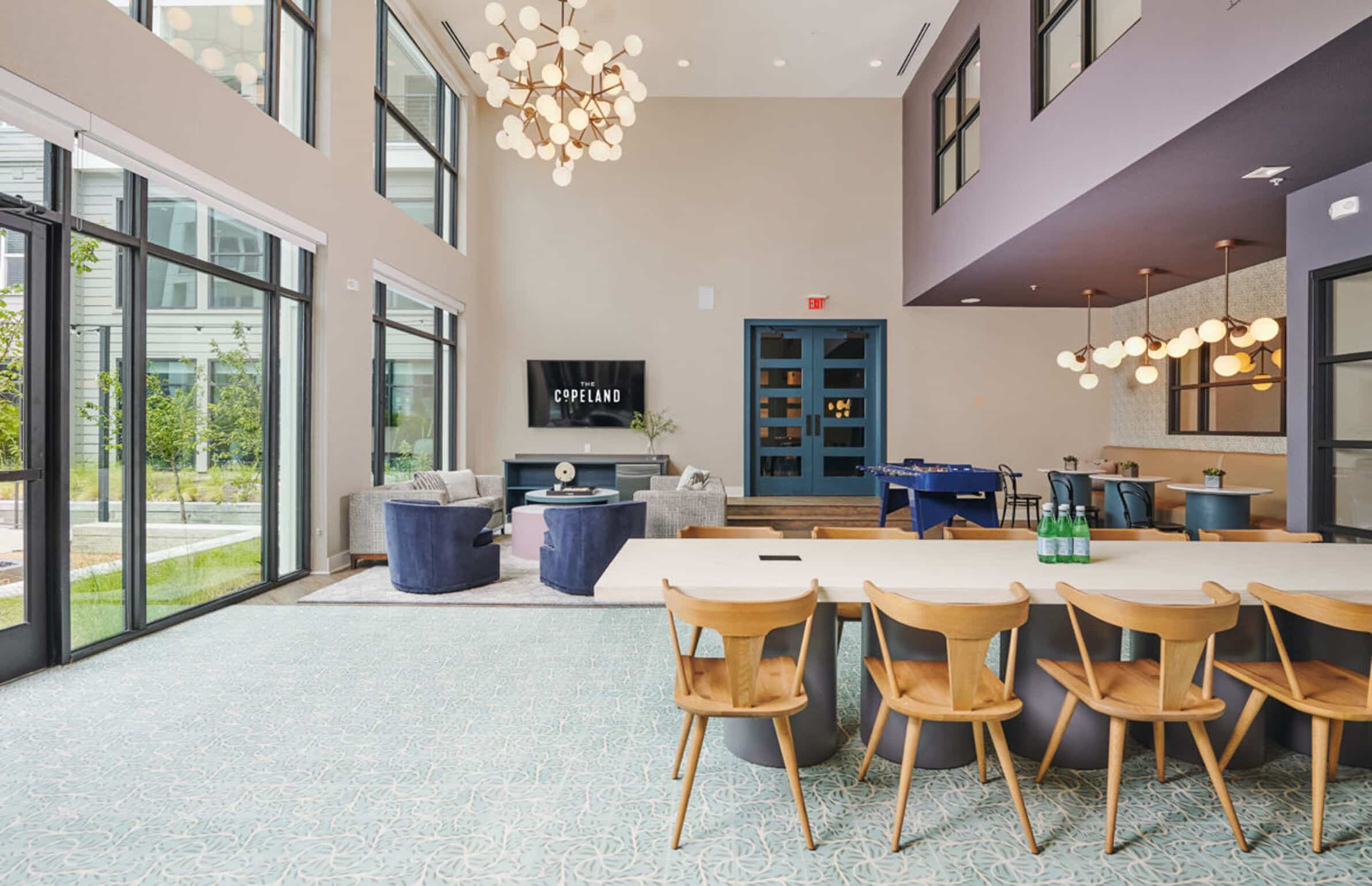 The Copeland lounge with large windows, seating areas, a TV, foosball table, and dining table with wooden chairs.