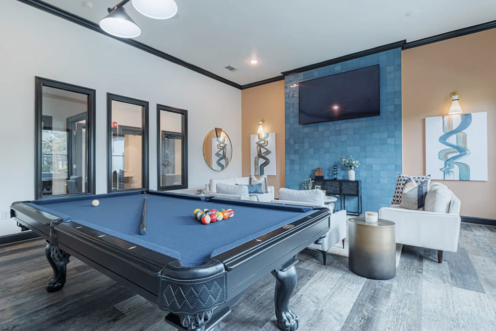 A The Bryx at Kingwood lounge with a blue pool table, white sofas, wall art, and a TV mounted above a blue accent wall.