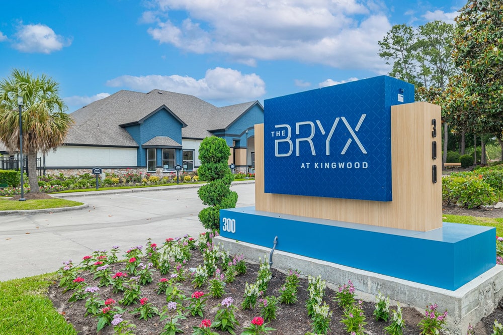 Large blue sign reading The Bryx at Kingwood, surrounded by flowers and greenery.