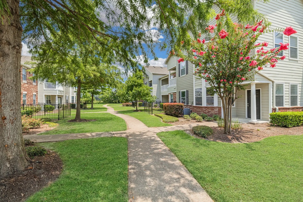Pathway through The Bryx at Kingwood with green lawns, trees, bushes, and blooming flowers.