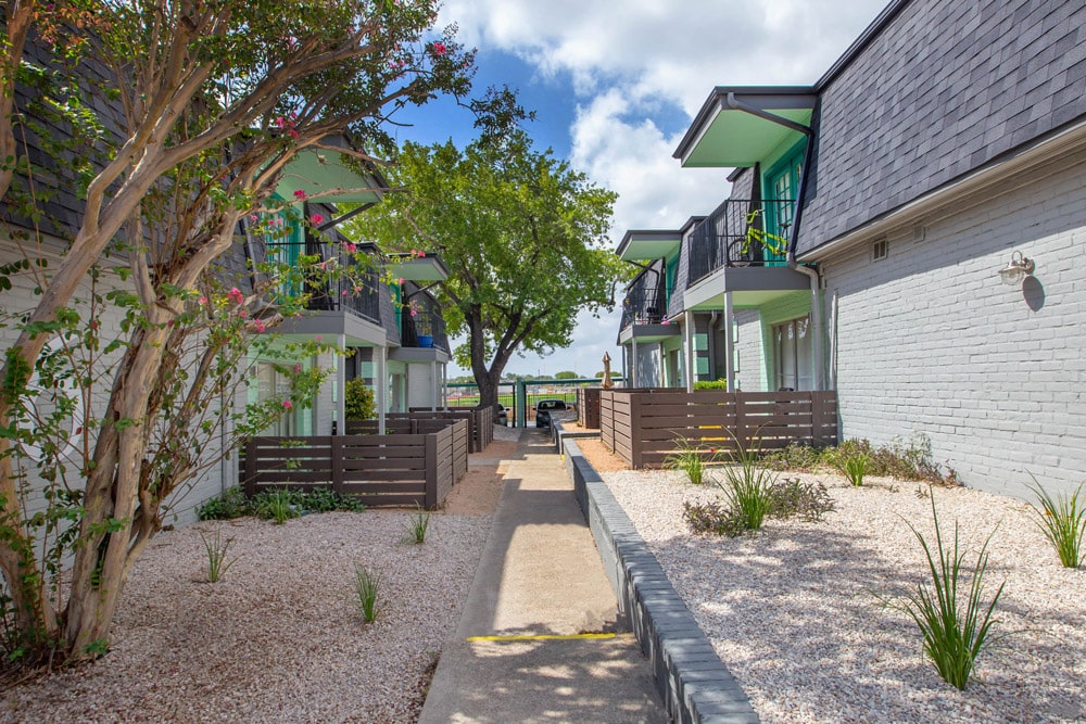 A walkway between modern townhomes at The Jackson with balconies, trees, and landscaped gravel gardens under a partly cloudy sky.