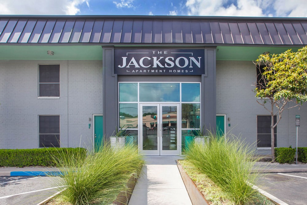 Entrance of The Jackson with large glass doors, sign above, and landscaped walkway in front.