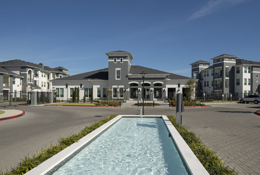 The Parkway on Westlake complex with a central fountain, gray buildings, and clear blue sky in the background.