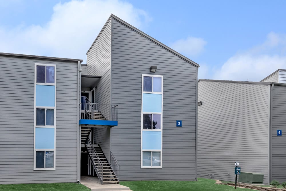 Modern gray apartment building at The Keller with tall windows, exterior stairs, and blue sky in the background.