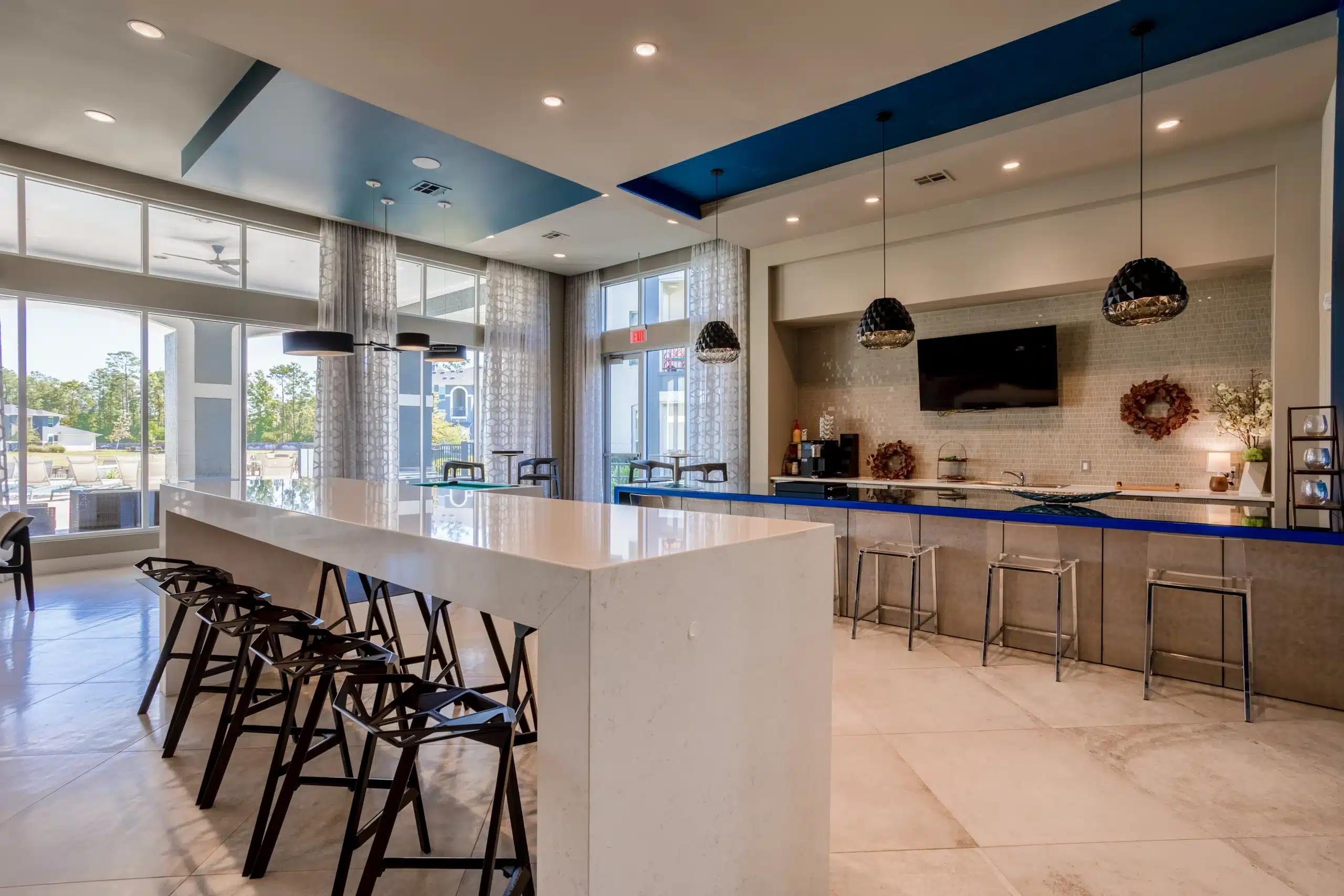 Modern communal kitchen at The Parkway on Westlake with high ceilings, long island, barstools, and large windows letting in natural light.
